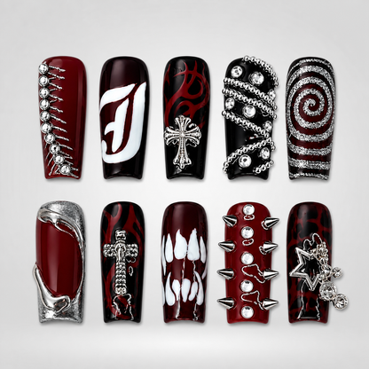 Ten glossy deep wine red and black press-on nails arranged on white, featuring red flames, silver crosses, chains, spikes, rhinestones, white graphics, and a star charm.