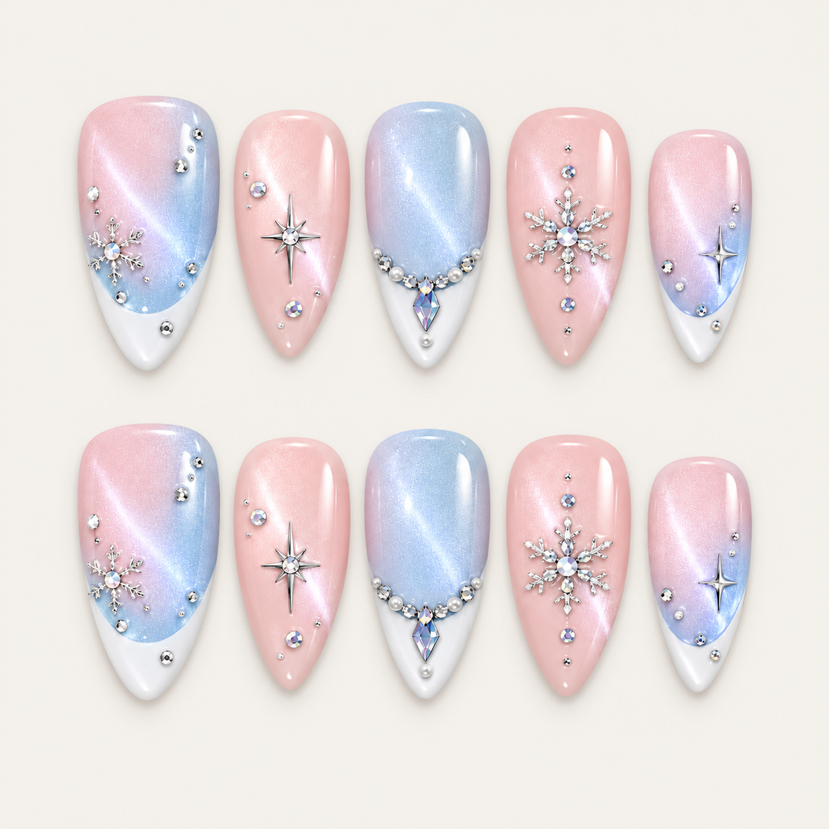 Ten blush pink and icy blue nails arranged in two rows on a greige background, featuring white tips, silver-toned snowflakes, starbursts, and jeweled accents.
