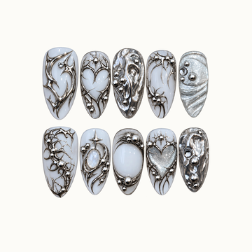Ten milky white and silver nails arranged in two rows on a light background, featuring chrome swirls, starbursts, hearts, and bead-like accents.
