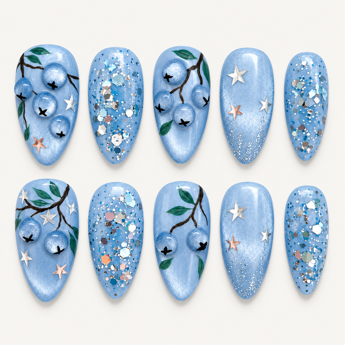 Ten pale blue nails arranged in two rows on a light neutral background, featuring blueberries, green leaves, stars, and reflective glitter.