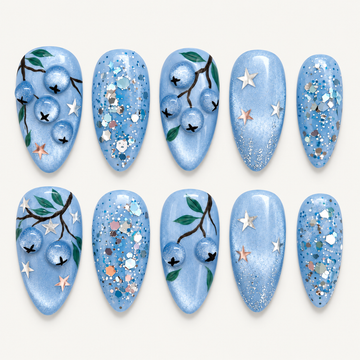Ten pale blue nails arranged in two rows on a light neutral background, featuring blueberries, green leaves, stars, and reflective glitter.