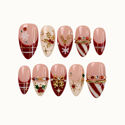 Ten Christmas press-on nails arranged in two rows on a pale neutral background, with ruby glitter tips, blush and ivory bases, snowflakes, holly, and gold-tone ornaments.