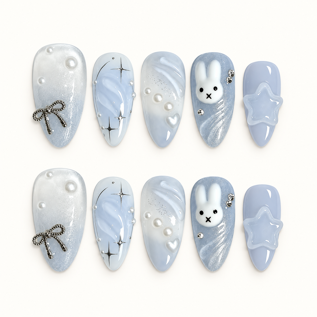 Ten pale blue and pearly white press-on nails arranged in two rows, featuring a bunny face, silver starbursts, pearls, a bow, and a raised star.