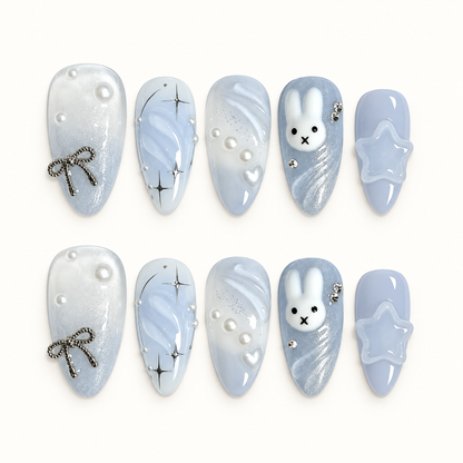 Ten pale blue and pearly white press-on nails arranged in two rows, featuring a bunny face, silver starbursts, pearls, a bow, and a raised star.