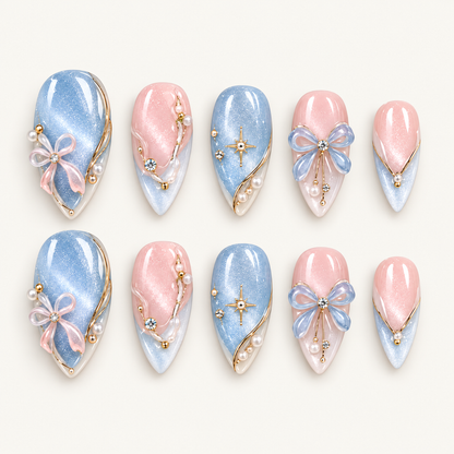 Ten pink and icy blue shimmering nails arranged in two rows on a light neutral background, decorated with raised bows, gold-tone starbursts, and pearl-like beads.