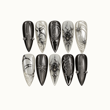 Ten pointed nails arranged in two rows on a light neutral background, featuring charcoal shimmer, pearly swirls, silver-tone loops, starbursts, and dark oval accents.