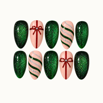 Ten nails arranged in two rows on a light neutral background, featuring emerald glitter, blush pink bases, red gift bows, and green and silver curved stripes.