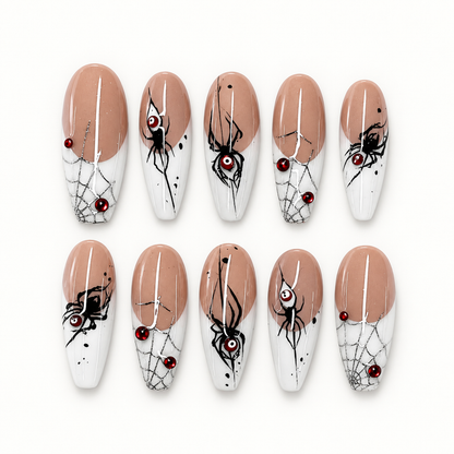 Ten glossy greige and pale-tip press-on nails with black spider silhouettes, cobweb linework, and deep red gem-like accents.