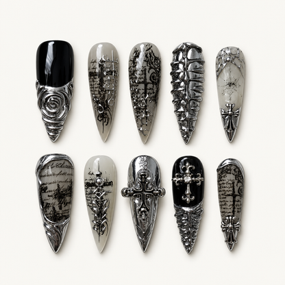 Ten coordinated gothic press-on nails displayed on a textured gray surface, with black, smoky gray, and silver chrome-look cross and rose details.