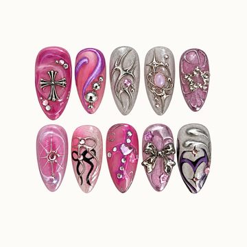 Ten coordinated pink, lilac, mauve, and silver nails arranged in two rows on a light background, with cross, bow, starburst, orbital, and gem accents.