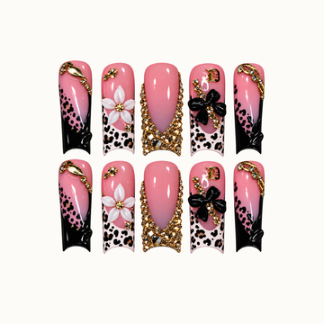 Ten pink nails arranged in two rows on a light background, featuring leopard spots, black tips, raised flowers, and gold-tone embellishments.