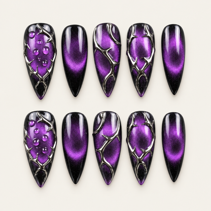 Ten violet-purple and black press-on nails displayed in a clear case, with raised dark chrome-like thornwork and droplet accents.