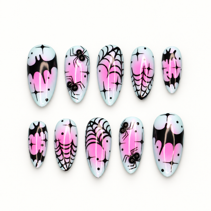 Ten glossy press-on nails with black spiderwebs, spiders, bright pink drips, dots, and starbursts on a pale base