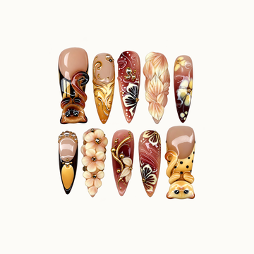 Ten coordinated nails in two rows on a light neutral background, featuring raised cats, cream flowers, amber accents, and gold-colored scrollwork.