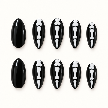 Black press-on nails with white skeletal bone motifs displayed against a soft greige background.