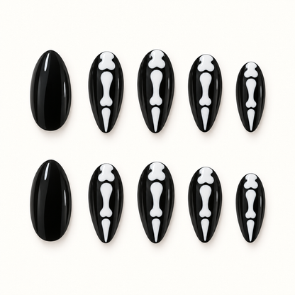 Black press-on nails with white skeletal bone motifs displayed against a soft greige background.