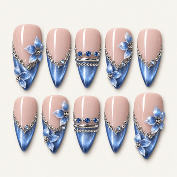 Ten blush pink and shimmering blue nails arranged in two rows, with blue petal accents, silver-toned chains, and blue gems.