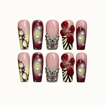 Ten coordinated nails arranged in two rows on a light neutral background, featuring blush pink, burgundy gradients, red flowers, raised droplets, and silver-tone accents.