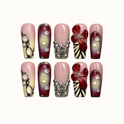 Ten coordinated nails arranged in two rows on a light neutral background, featuring blush pink, burgundy gradients, red flowers, raised droplets, and silver-tone accents.