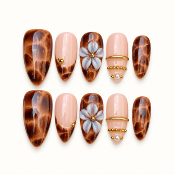 Ten nails arranged in two rows on a light background, featuring amber-brown marbling, blush pink accents, raised pale flowers, and gold-tone details.