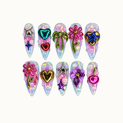 Ten pointed nails in two rows on a light neutral background, with pastel iridescent bases, raised bubbles, metallic flowers, hearts, bows, stars, and a cherry.
