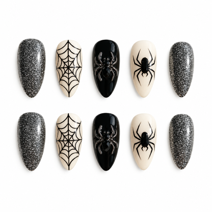 Ten coordinated press-on nails in silver glitter, glossy black, and ivory with black spiderweb and spider accents arranged in two rows.