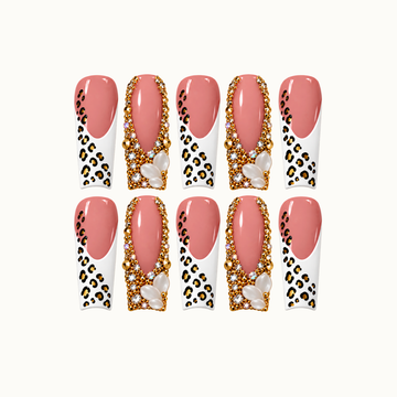 Ten blush pink nails arranged in two rows on a light background, alternating white leopard-print tips with gold-tone jeweled borders and pearl-like clusters.