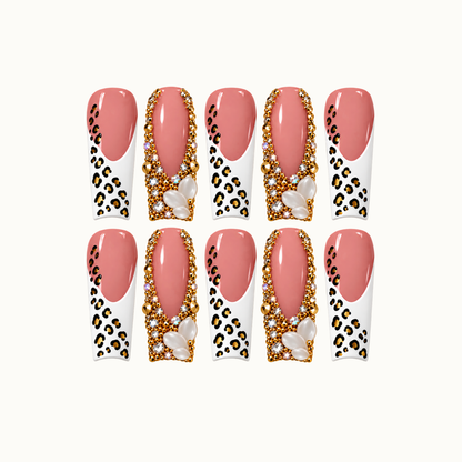 Ten blush pink nails arranged in two rows on a light background, alternating white leopard-print tips with gold-tone jeweled borders and pearl-like clusters.