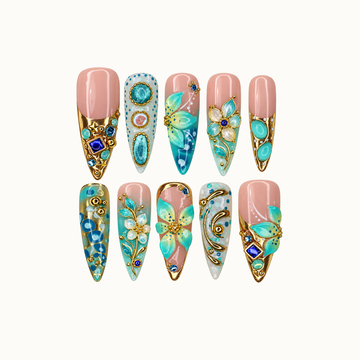 Ten decorated nails arranged in two rows on a light neutral background, featuring blush pink, turquoise flowers, gold-tone scrollwork, and blue jewel-like accents.