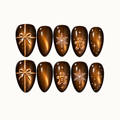 Ten glossy brown and amber shimmer nails in two rows, featuring gold-toned gift bows, white snowflakes, gingerbread figures, and stars on a light neutral background.