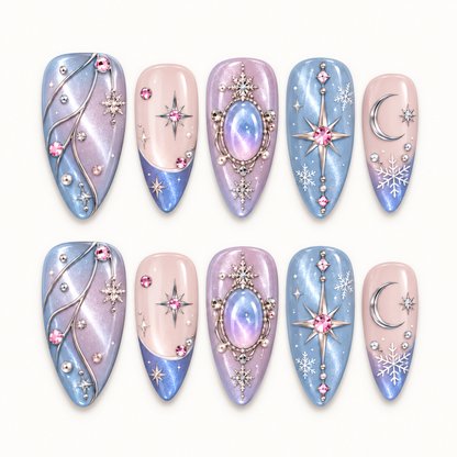 Ten pastel blue, lilac, and blush pink nails arranged in two rows, decorated with moons, stars, snowflakes, and jewel-like accents on a light background.