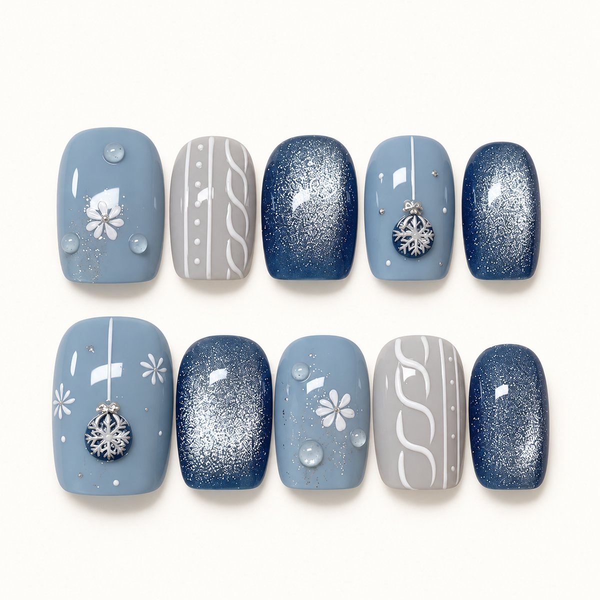 Ten coordinated nails arranged in two rows on a pale background, featuring dusty blue florals and snowflake ornaments, navy shimmer, and gray knit-inspired accents.