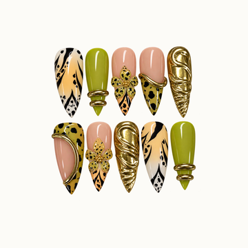 Ten coordinated nails in two rows on a light neutral background, featuring chartreuse green, nude pink, spotted flowers, black patterns, and sculptural gold-tone accents.