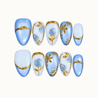 Ten blue and pale blue nails arranged in two rows on a light background, featuring gold-outlined roses, gold leaves, petal clusters, and curved bands.