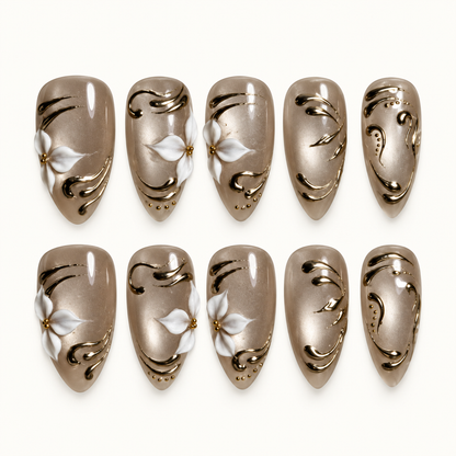 Ten glossy taupe-greige nails arranged in two rows on a light background, featuring white floral accents, gold-tone swirls, and small decorative dots.