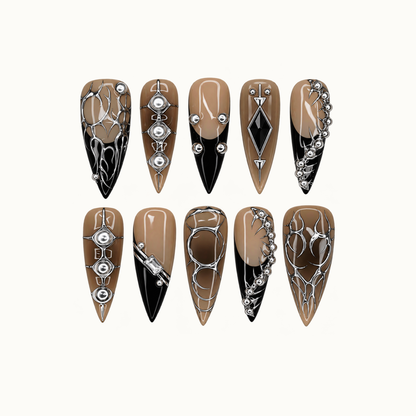 Ten pointed nails in two rows on a light background, featuring taupe and black sections, silver-tone thorn motifs, rounded accents, and geometric details.