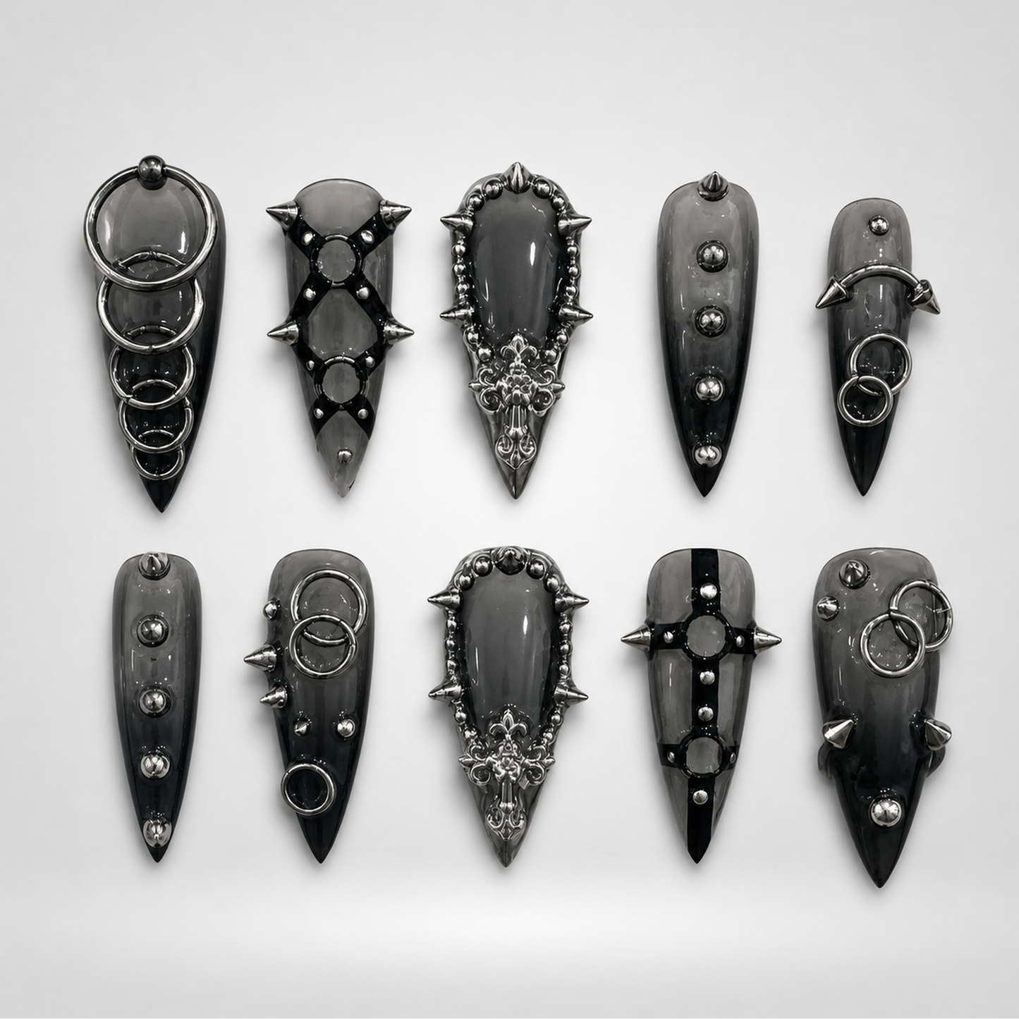 Ten glossy charcoal-black gothic press-on nails arranged in two rows, featuring silver-toned rings, studs, spikes, and ornate raised details.