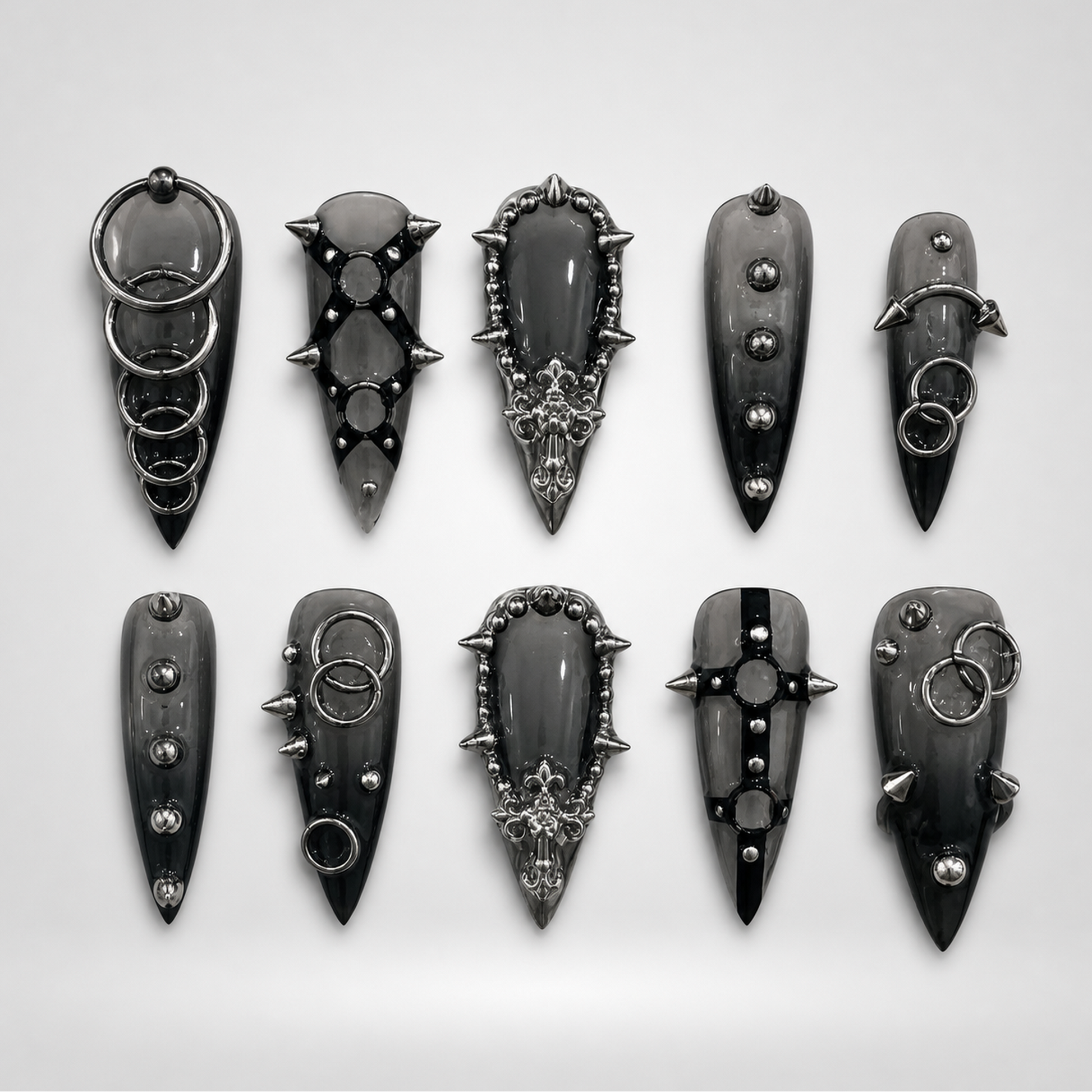 Ten glossy charcoal-black gothic press-on nails arranged in two rows, featuring silver-toned rings, studs, spikes, and ornate raised details.