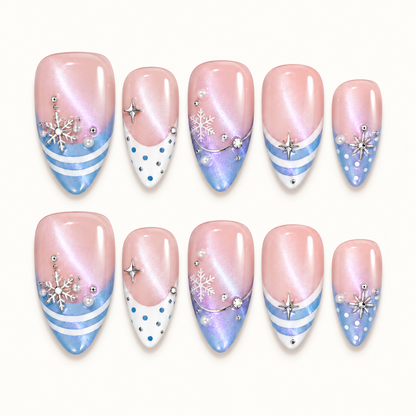 Ten blush pink shimmer nails arranged in two rows on a light neutral background, with icy blue tips, white stripes and dots, snowflakes, and silver-toned accents.