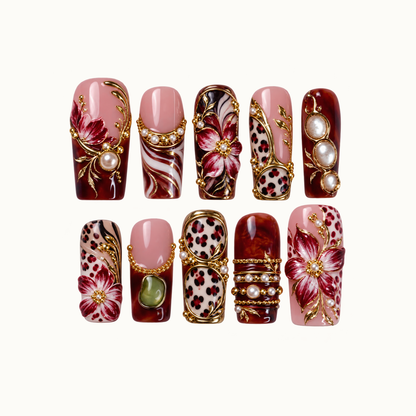 Ten decorated nails arranged in two rows on a light background, with burgundy flowers, blush pink panels, leopard spots, gold-tone details, and pearl-like accents.