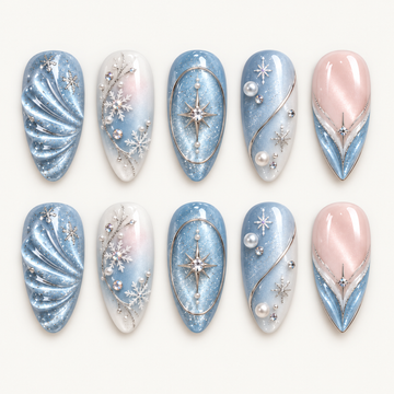 Ten glossy nails arranged in two rows on a light neutral background, featuring icy blue, white, and blush pink with snowflakes, starbursts, and pearl-like accents.