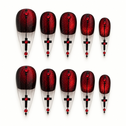 Crimson red glitter press-on nail set with black edging, clear pointed tips, black cross-inspired details, and red gem-like accents.