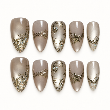 Ten glossy greige and champagne nails arranged in two rows on a light background, with gold-toned floral scrollwork and iridescent tip accents.