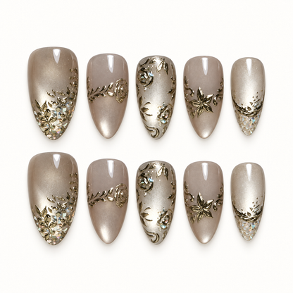 Ten glossy greige and champagne nails arranged in two rows on a light background, with gold-toned floral scrollwork and iridescent tip accents.