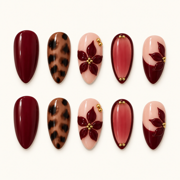 Ten glossy nails arranged in two rows on a light neutral background, featuring burgundy solids, leopard spots, blush floral accents, and gold-tone beads.