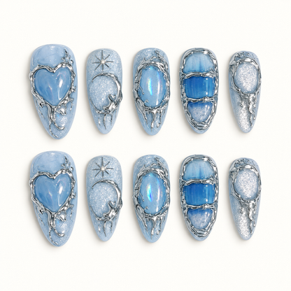 Ten icy blue press-on nails arranged in two rows, showing a glossy heart, crescent and star, iridescent oval, blue panels, and silver-tone outlines.