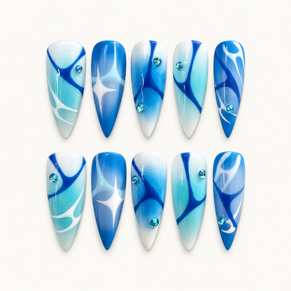 Ten coordinated blue abstract press-on nails with aqua gradients, white curved accents, and faceted gem details arranged on a display card.