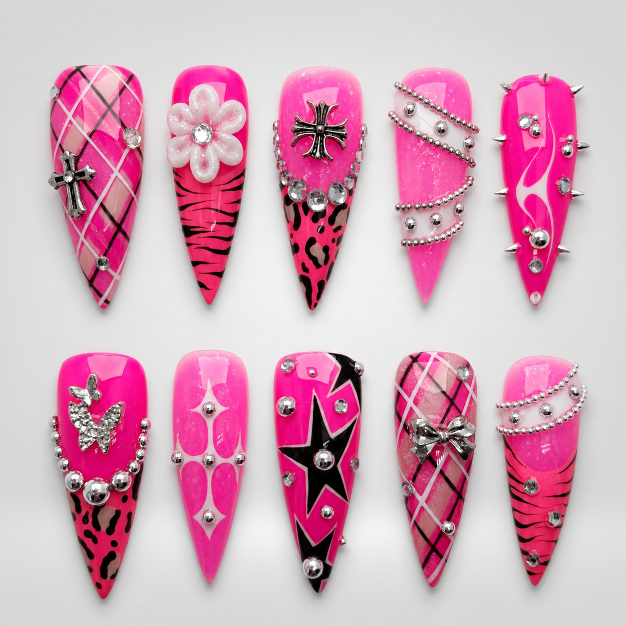 Ten coordinated hot-pink press-on nails displayed in two rows, featuring plaid, stripes, animal-inspired spots, stars, silver-toned charms, studs, and bead-chain accents.