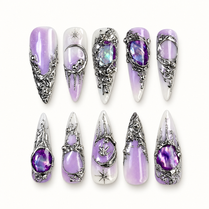 Ten violet, white, and deep purple marbled press-on nails displayed in a clear case with ornate silver-toned raised embellishments and gem-like accents.