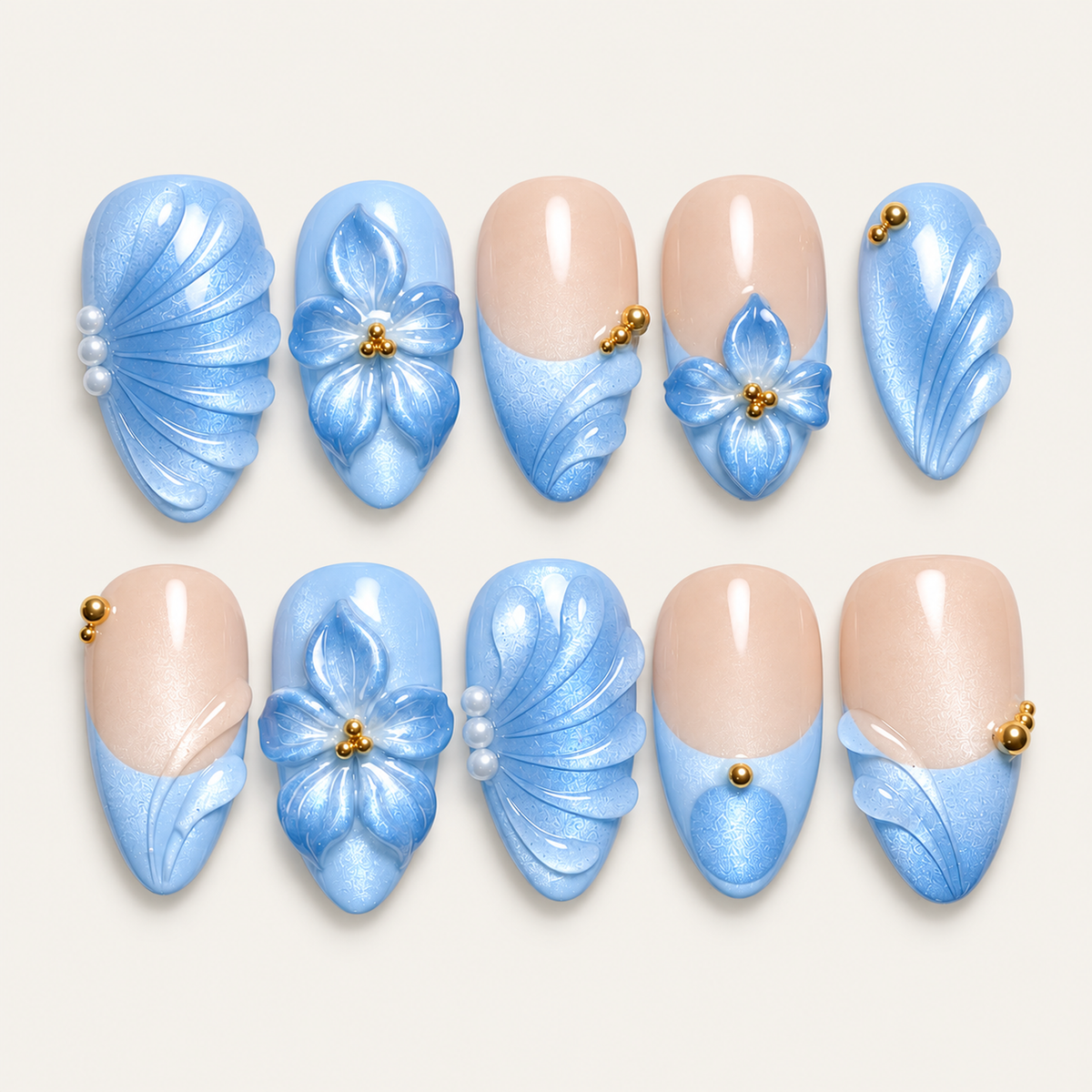 Ten pale blue and nude press-on nails arranged in two rows, with blue flowers, fan-like curves, pearl-like accents, and gold-tone beads on a light background.